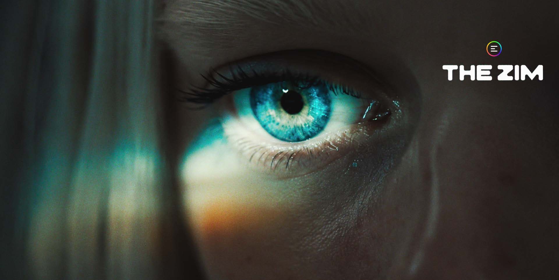 Extreme close-up of a young woman's eye, the iris a vivid cyan-blue lit from the front with a small white catchlight and a dark pupil; long dark lashes above and below, the tear duct and lower lid catching a glint of moi